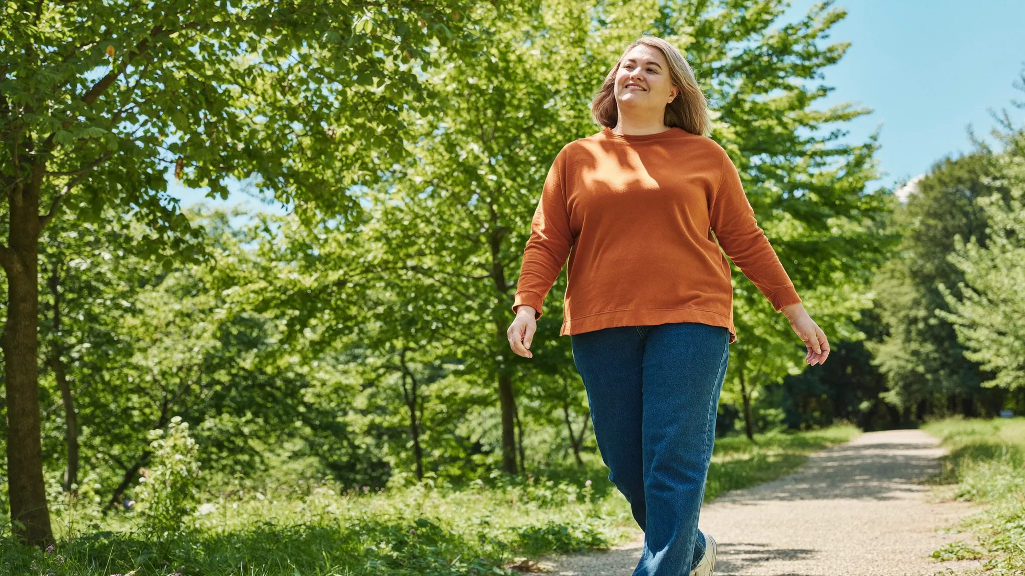 A woman on an easy everyday walk along a sunlit tree-lined park path